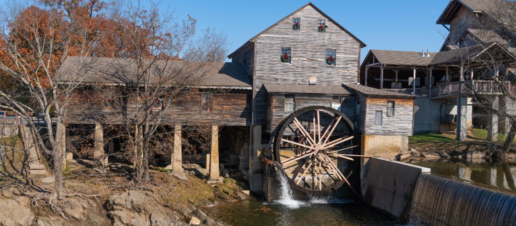 A distant view of The Old Mill Restaurant, showing the mill turn the water and balcony seating overlooking the Little Pigeon River.